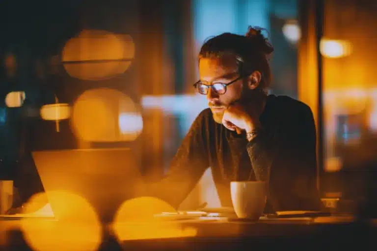 Focused marketer working late on a laptop in a warm, softly lit office with coffee on the desk.