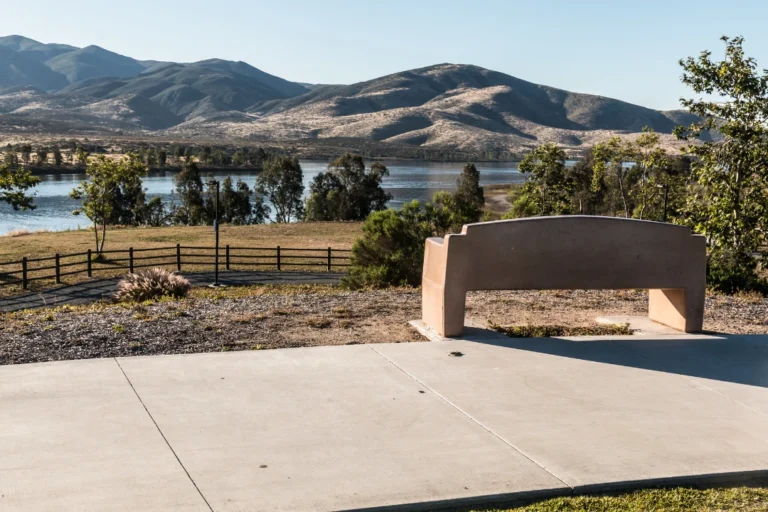 Scenic overlook in Otay Ranch featuring rolling hills, a peaceful lake, open green space, and a modern bench with mountain views.